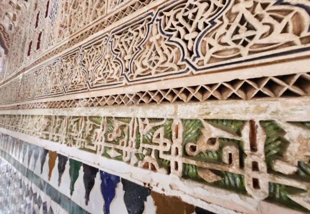 Close-up of carved stucco with Arabic calligraphy above green and blue zellige at Bahia Palace