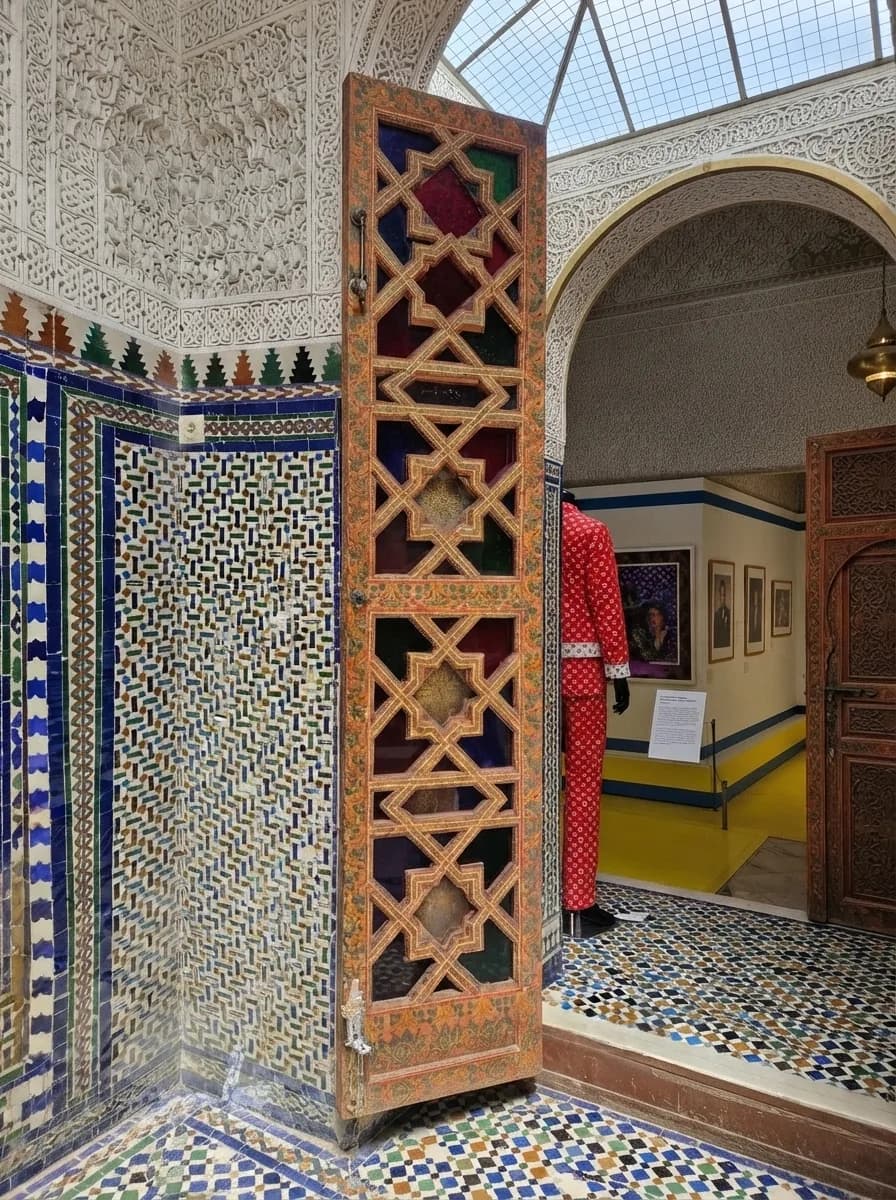 Carved wooden lattice screen beside zellige tiled walls in an interior room of Bahia Palace