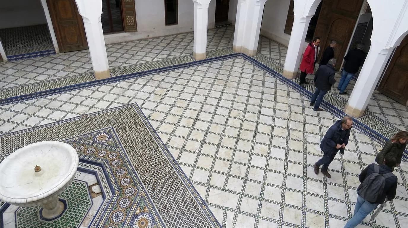 Visitors walking across the white marble and zellige courtyard floor of Bahia Palace
