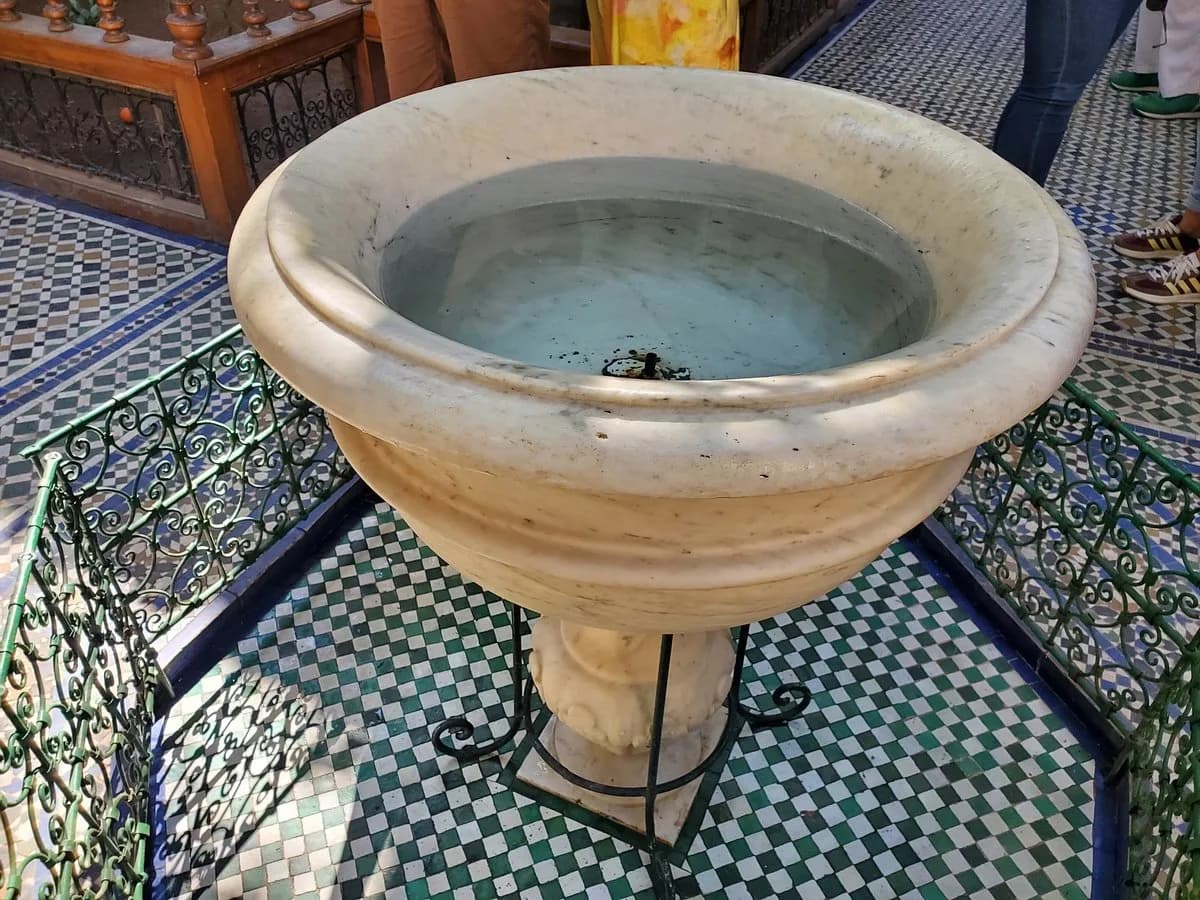 Close-up of a carved marble fountain basin surrounded by green ironwork at Bahia Palace