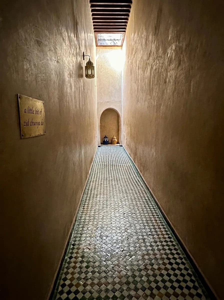 Narrow tadelakt corridor with a chequered zellige floor and wall lantern at Bahia Palace