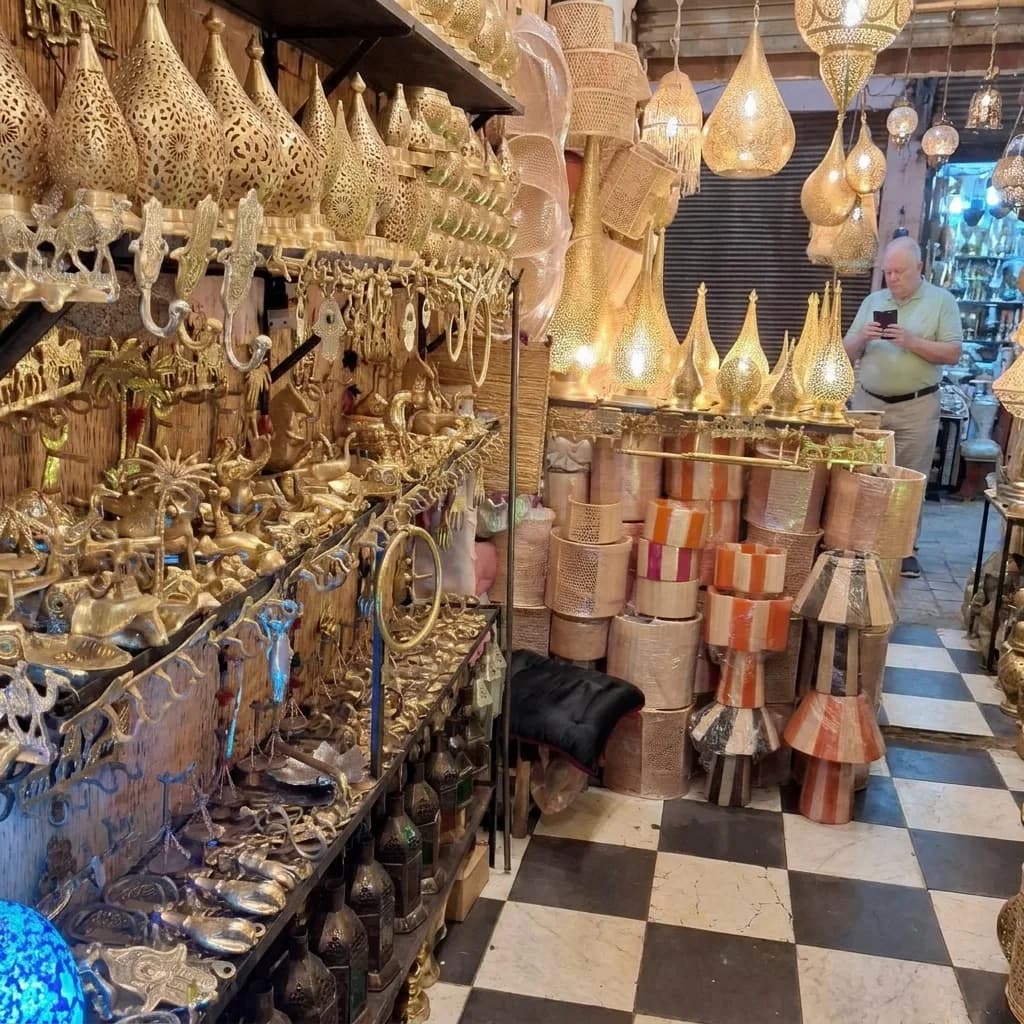 Brass lanterns, copper vessels and metalwork filling a workshop stall in the Marrakech souk — Palais de la Bahia Marrakech