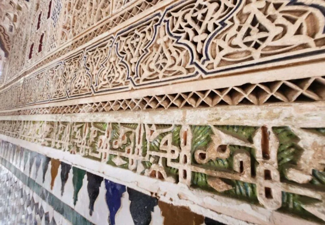 Arabic calligraphy carved in plaster stucco above intricate zellige mosaic tilework in the interior courtyard of Bahia Palace Marrakech