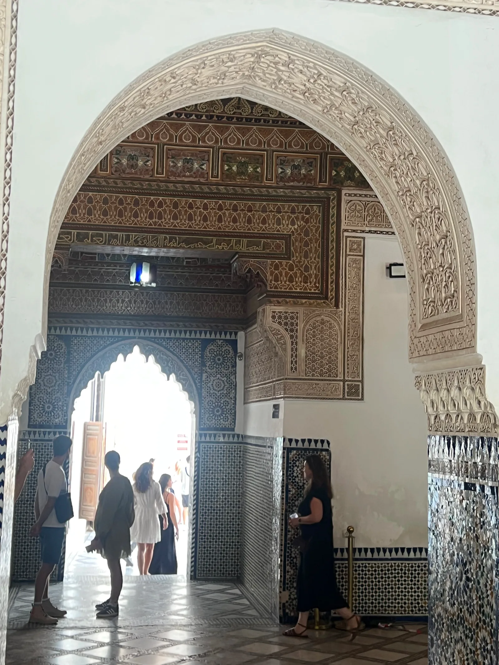 زوار يمرون عبر قوس جبصي منحوت مزخرف بالزليج داخل قصر الباهية بمراكش يُظهر تجربة الزائر في الداخل