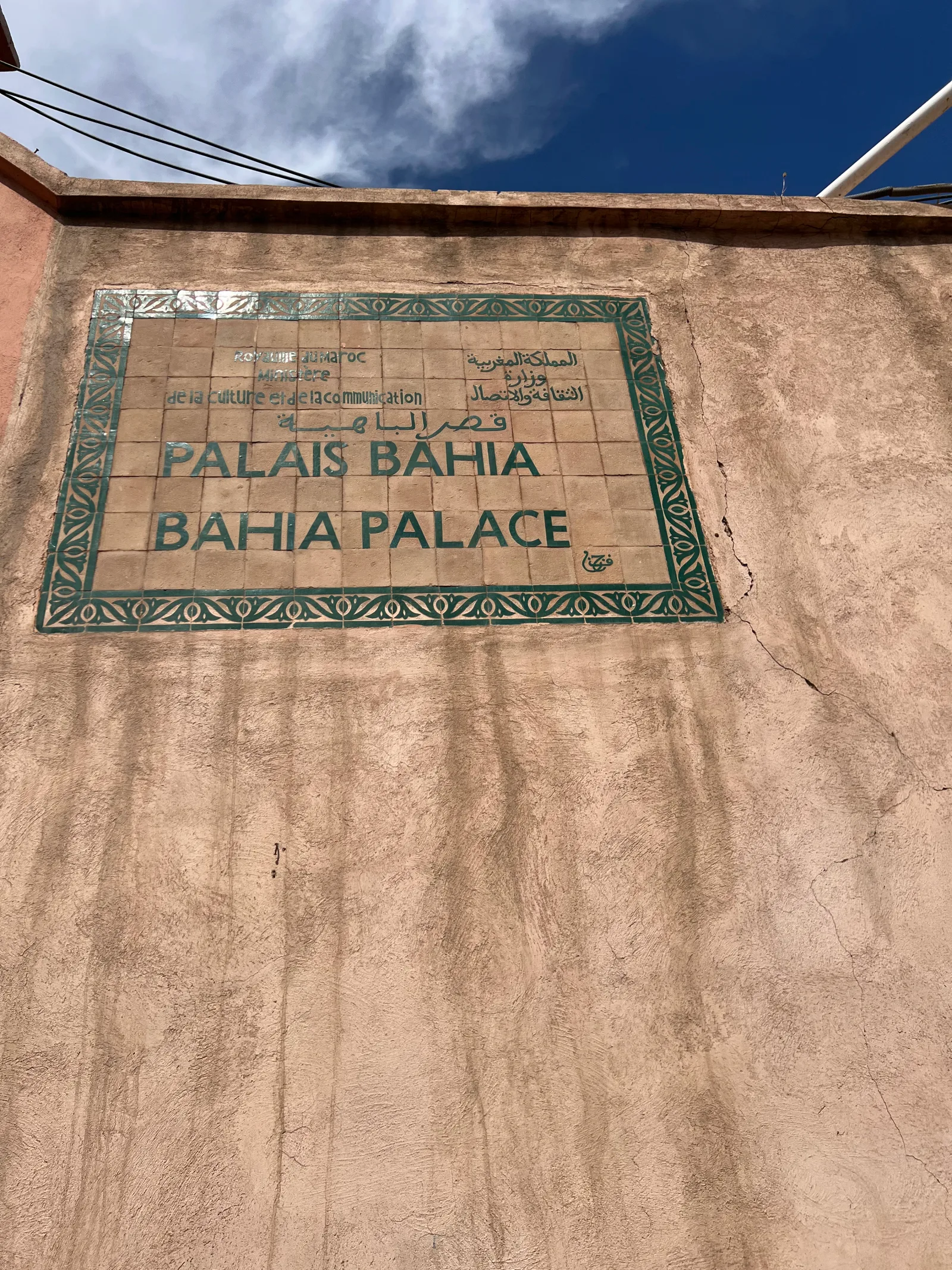 اللافتة الخارجية الرسمية المزيّنة بالزليج لقصر الباهية مكتوب عليها Palais Bahia وقصر الباهية بالفرنسية والعربية والإنجليزية مثبتة على الجدار الخارجي